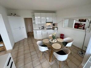 A compact kitchen with white cabinets, a dining table with four chairs, and a small island with a plant. - Seehütte Ferienwohnung 702 (Cuxhaven)