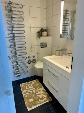 A modern bathroom with a white sink, a toilet, and a shower with a metal rack. - Seehütte Ferienwohnung 702 (Cuxhaven)