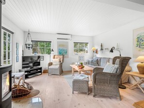 Un salon spacieux avec une cheminée, des meubles en osier, un téléviseur et un coin repas.