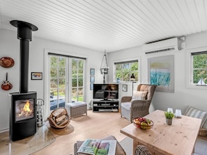A modern living room with a wood-burning stove, large windows, a television, and comfortable seating.