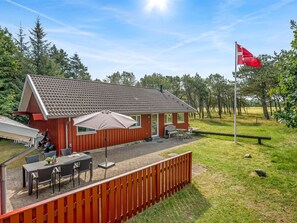 A red building with a tiled roof, a patio with outdoor furniture, and a flagpole with a flag.
