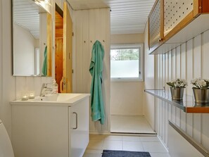 Ein Badezimmer mit weißem Waschtisch, einem Spiegel, einem Fenster und einem Regal mit Topfpflanzen.
