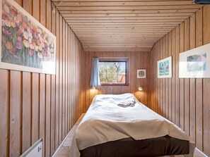 Ein schmaler Raum mit Holzwänden, einem Einzelbett, einem Fenster mit Blick und Bildern an den Wänden.