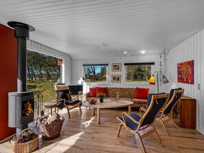 A cozy living room with a fireplace, comfortable seating, and large windows offering a view of the outdoors.