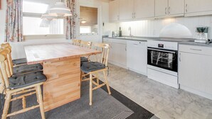 A modern kitchen with white cabinets, a wooden dining table, and a built-in oven.