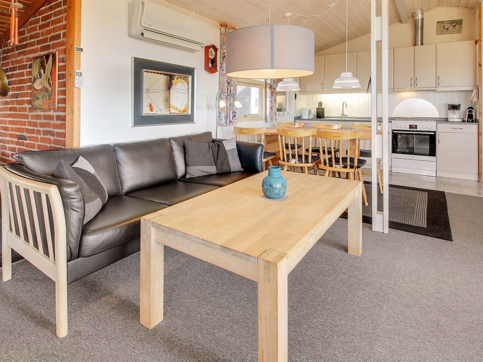 A modern living room with a leather sofa, a wooden coffee table, and a dining area with wooden chairs and a white table.