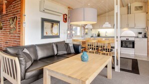 A modern living room with a leather sofa, a wooden coffee table, and a dining area with wooden chairs and a white table.