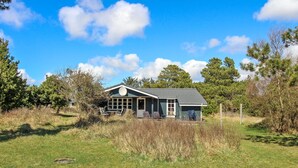 Une maison dotée d’une grande véranda, d’une fenêtre ronde et d’un espace extérieur aménagé et abrité.