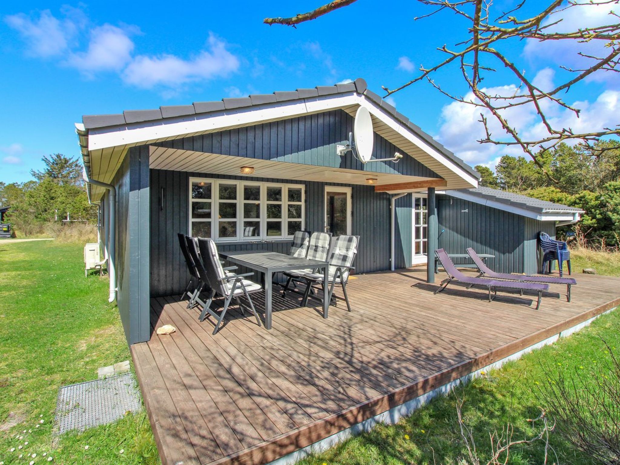 Une maison moderne dotée d’une terrasse, d’un coin repas avec des chaises et d’un espace détente avec un fauteuil.