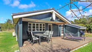 Une maison moderne dotée d’une terrasse, d’un coin repas avec des chaises et d’un espace détente avec un fauteuil.