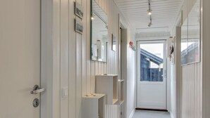 A hallway with white paneled walls, a door at the end, and a small shelf with items on it. - "Auli" - 200m from the sea by Interhome (Vejers Strand)