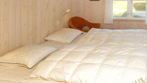 A bed with a white duvet and pillows, a wooden headboard, a bedside lamp, and a window with a view of greenery. - "Zuzan" - 500m from the sea by Interhome (Vejers Strand)