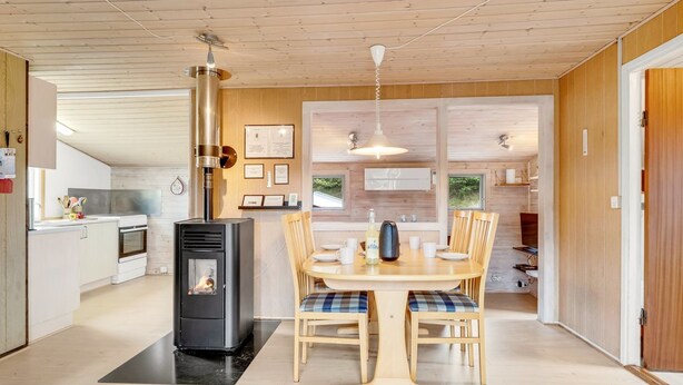 Eine moderne Küche mit Holzofen, einem Essbereich mit Tisch und Stühlen sowie Blick ins Freie.