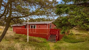 Eine rote Holzhütte mit einer Treppe, die zu einer Tür führt, umgeben von Gras und Bäumen.