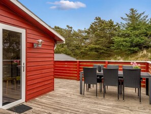 A red building with a glass door, a deck with outdoor furniture, and a view of trees.
