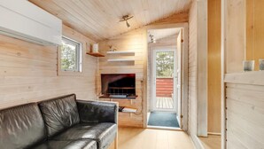 Ein modernes Blockhaus-Interieur mit Ledersofa, Fernseher und Holzbalkendecke.