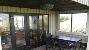 Un patio cubierto con suelo de ladrillo, una mesa con sillas y vistas al exterior a través de amplias ventanas.