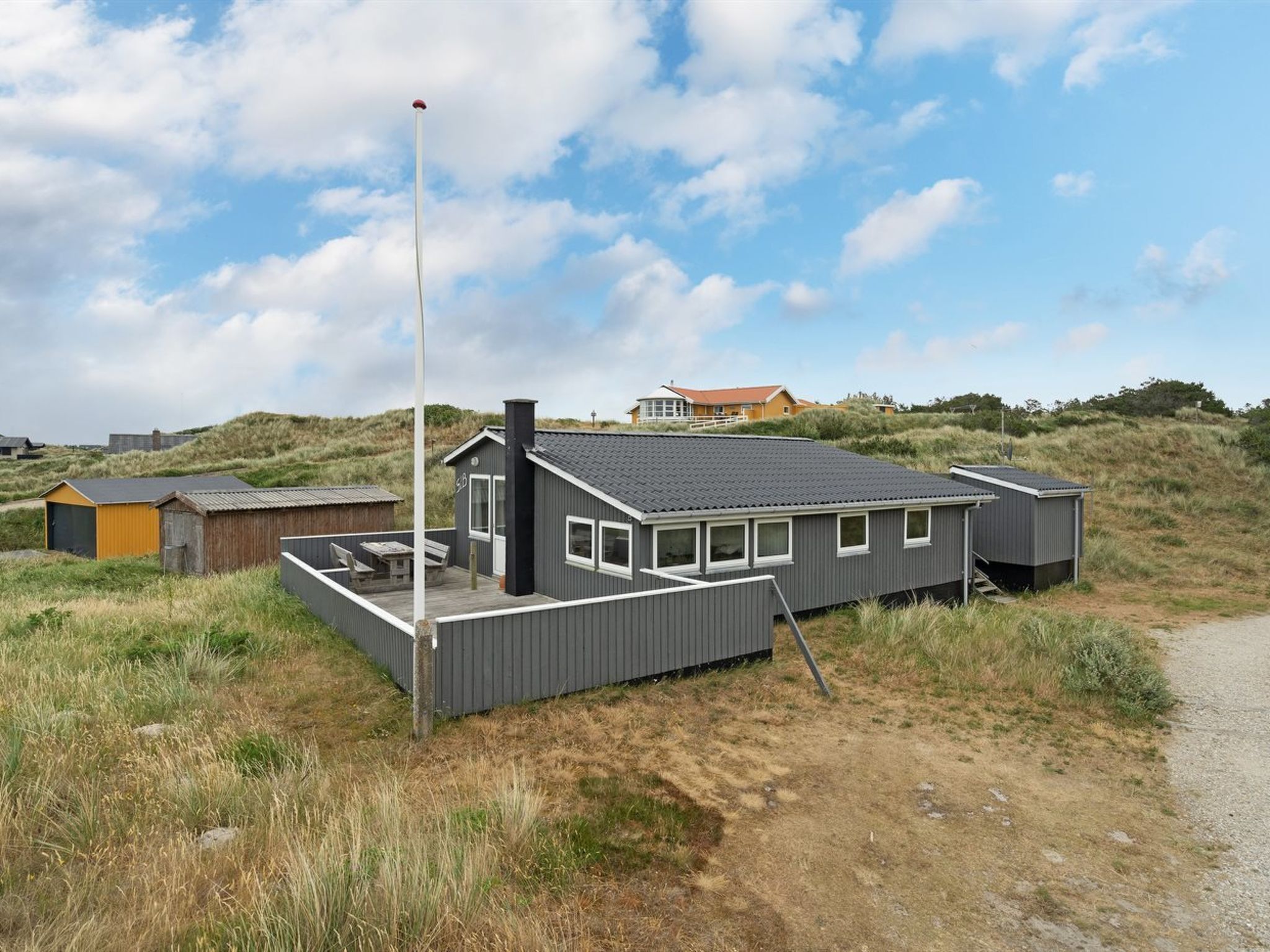 A modern, single-story house with a flat roof, a chimney, and a flagpole.
