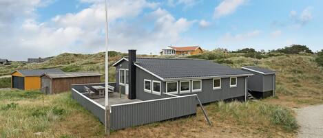 A modern, single-story house with a flat roof, a chimney, and a flagpole.