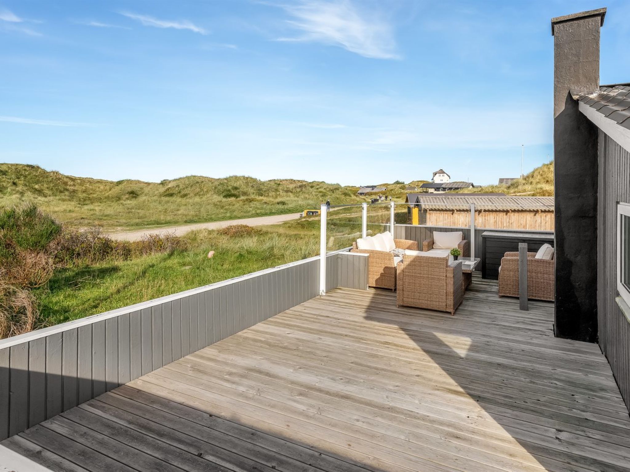 A wooden deck with outdoor furniture, a view of the landscape, and a building in the background.