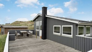A modern building with a grey exterior, numbered 23, featuring a deck with wooden furniture and a chimney.