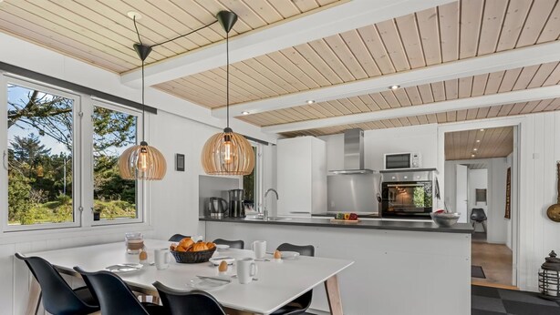 A modern kitchen with a central island, black chairs, and pendant lighting.
