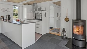 A modern kitchen with a central island, built-in oven, microwave, and stainless steel appliances. A wood-burning stove is visible in the background.