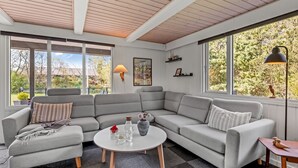 A modern living room with a grey sectional sofa, a round coffee table, and a large window offering a view of the outdoors.