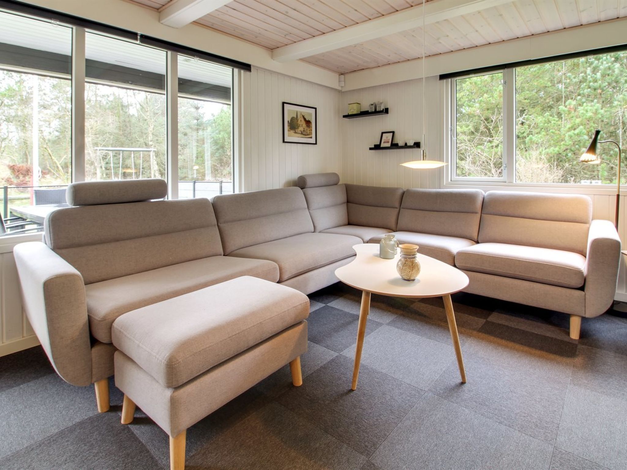 A modern living room with a sectional sofa, a round coffee table, and large windows offering a view of trees.