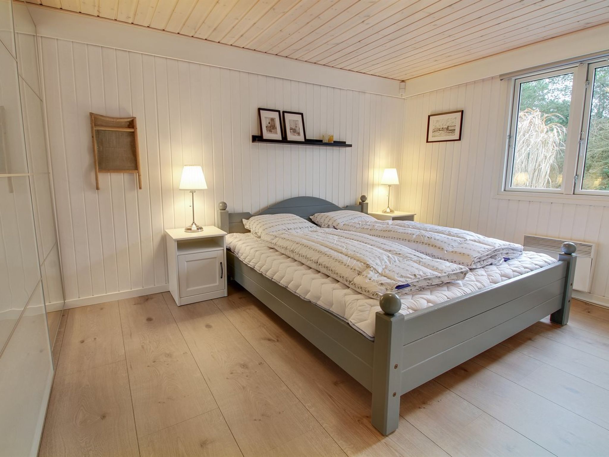 Une chambre à coucher comprenant un lit, deux tables de chevet, une fenêtre et des étagères fixées au mur.