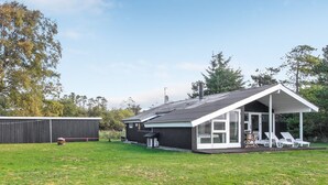 Ein modernes Haus mit überdachter Terrasse, umzäunter Garten und einem großen Baum im Hintergrund.