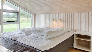 Ein Schlafzimmer mit einem großen Bett, einer Holzbalkendecke und einem Fenster mit Blick auf eine Wiese.
