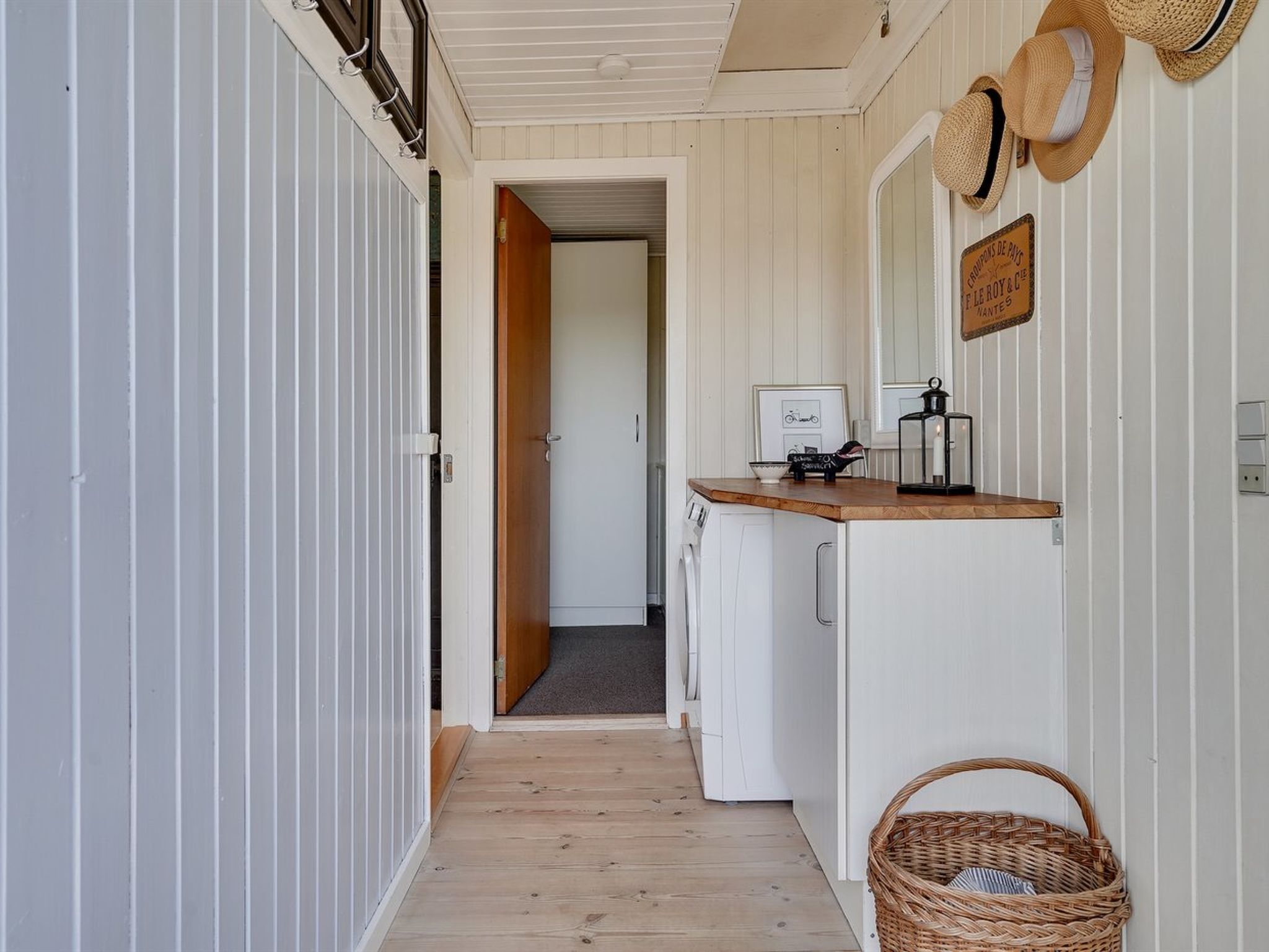 A narrow hallway with a wooden floor leading to a kitchen area with a wooden countertop and a washing machine.