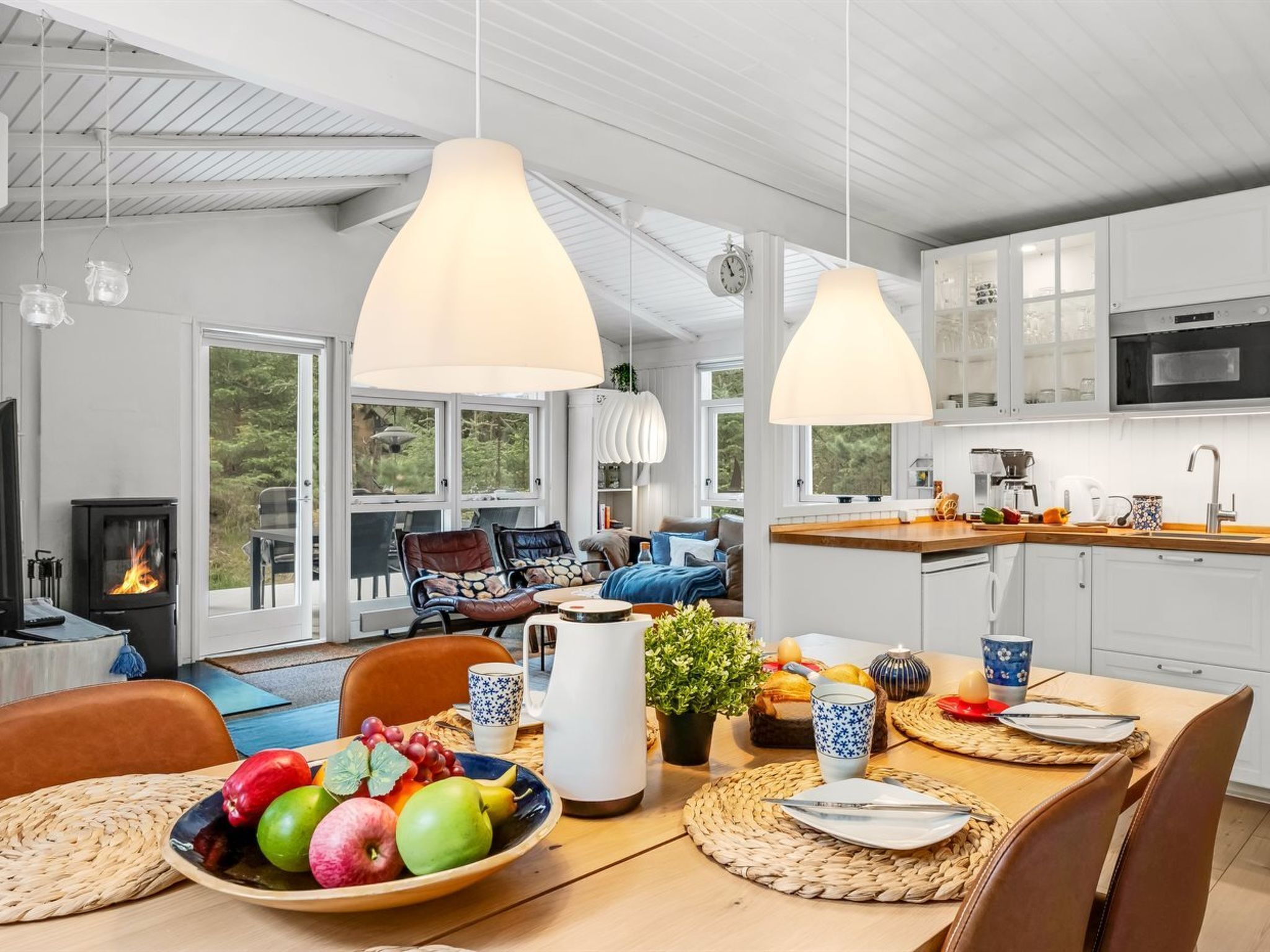 A modern kitchen with white cabinets, a built-in oven, and a dining area with a wooden table set for two.
