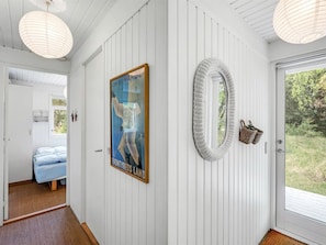 A hallway with a bed, a poster, a mirror, and a door leading outside.