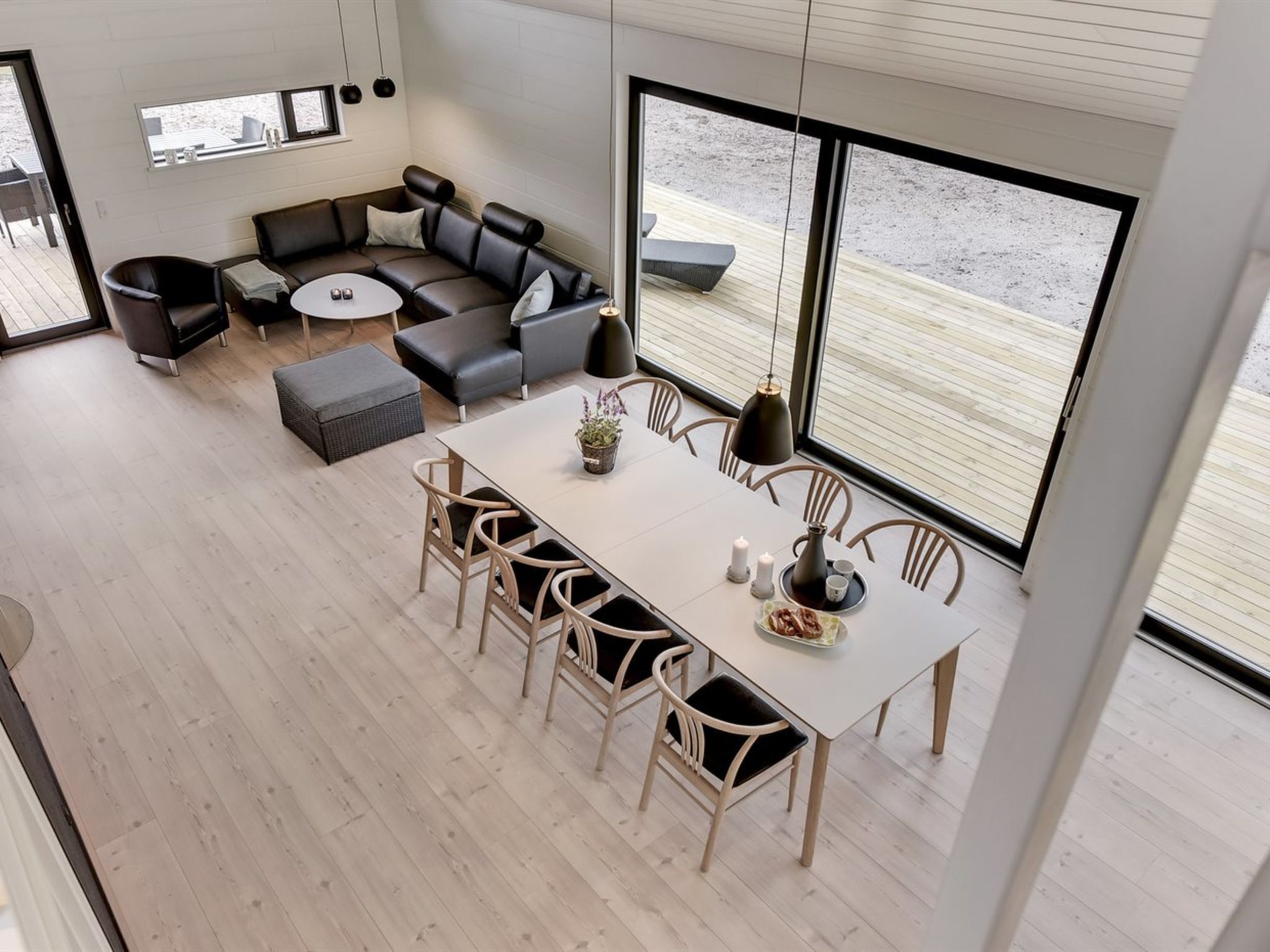 A modern living room with a large L-shaped sofa, a dining table with six chairs, and a large window providing a view of the deck.