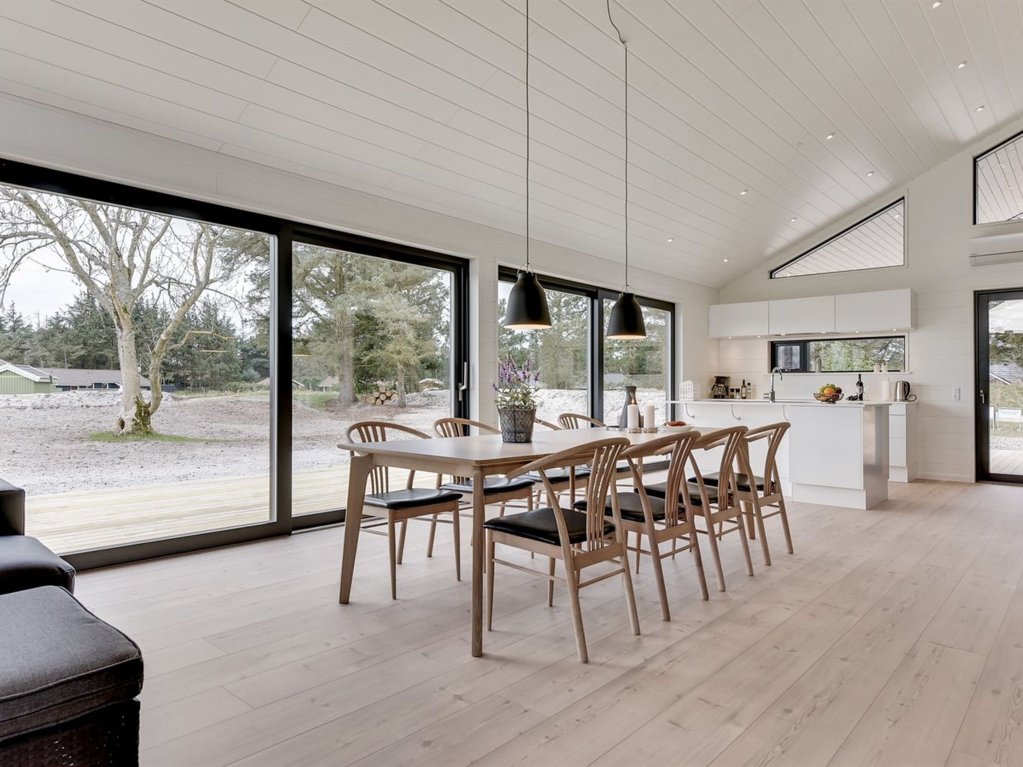 A modern kitchen with a dining area, large windows, and a view of the outdoors.