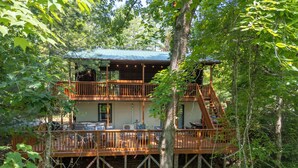 Une cabane en bois à deux étages, dotée d’un balcon et entourée d’arbres.