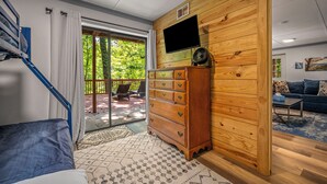 Une chambre moderne avec un mur en bois, un téléviseur à écran plat, une commode en bois, un canapé et un escalier menant à un balcon aménagé avec du mobilier d’extérieur.