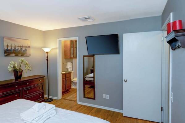 A hotel room with a bed, a dresser, a mirror, a TV, and a painting on the wall.
