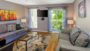 A living room with a sofa, coffee table, and TV, with a balcony and outdoor view. - Riverside Roost (Nashville)