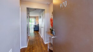 A hallway with a wooden floor, a door with the number 970, and a small table with a vase of flowers. - Riverside Roost (Nashville)