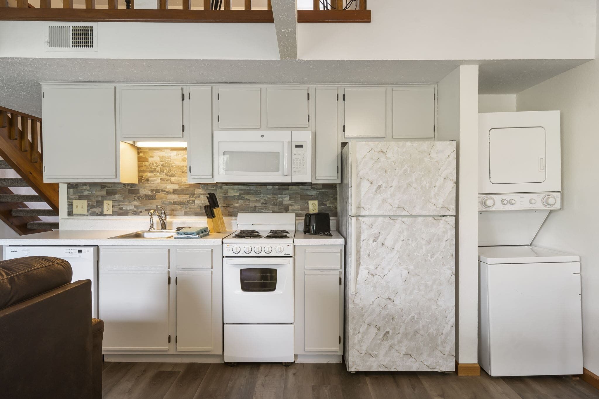 A compact kitchen with white cabinets, a microwave, a stove, a refrigerator, and a dishwasher.