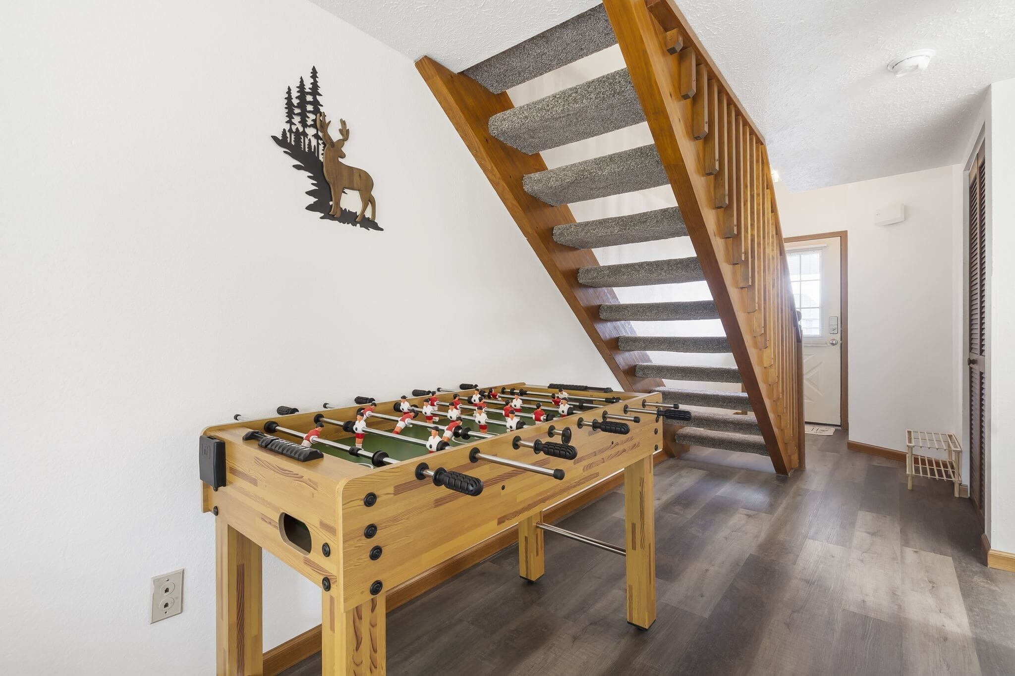 Ett rum med ett fotbollsspel, en trätrappa och en älgdekoration som hänger på väggen.