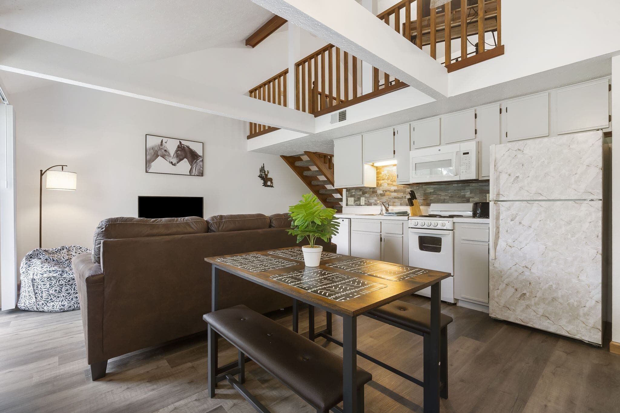 A modern kitchen with white cabinets, a marble refrigerator, and a dining area with a wooden table and bench.