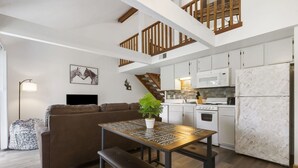 Una cocina moderna con armarios blancos, un refrigerador de mármol y un comedor con mesa y banco de madera.