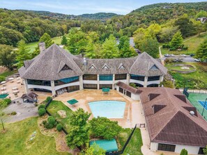 A large, multi-story building with a central courtyard, outdoor pool, and tennis court. - Retreat by Design - Resort Amenities (Branson West)