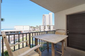 A balcony with a table and chairs, a view of the beach, and a tall building in the background. - Sea Forever Cozy Oceanfront Condo (Panama City Beach)