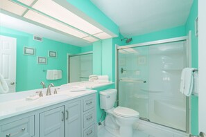 A bathroom with a white sink, toilet, and shower. There are framed pictures on the wall and a towel rack. - Sea Forever Cozy Oceanfront Condo (Panama City Beach)