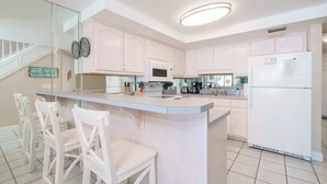 Eine moderne Küche mit weißen Schränken, einer zentralen Kochinsel mit Barhocker, einer eingebauten Mikrowelle und einem Kühlschrank mit Notiz.